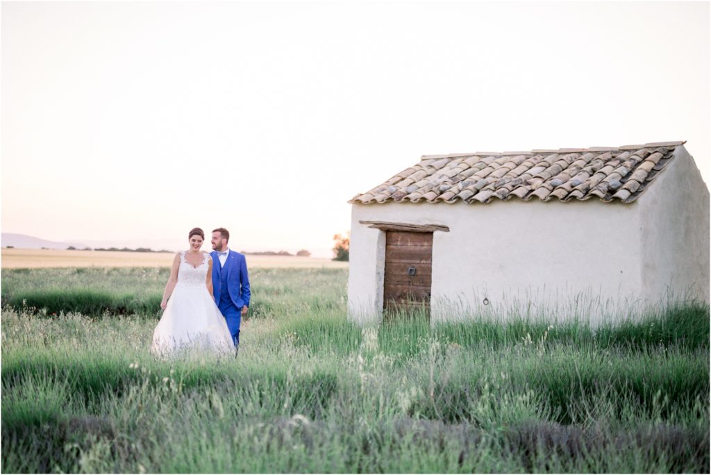 Seance photo de couple lors du mariage de Lara et Joao dans un champs de lavande. Les mariés marchent à côté d'un cabanon provencal