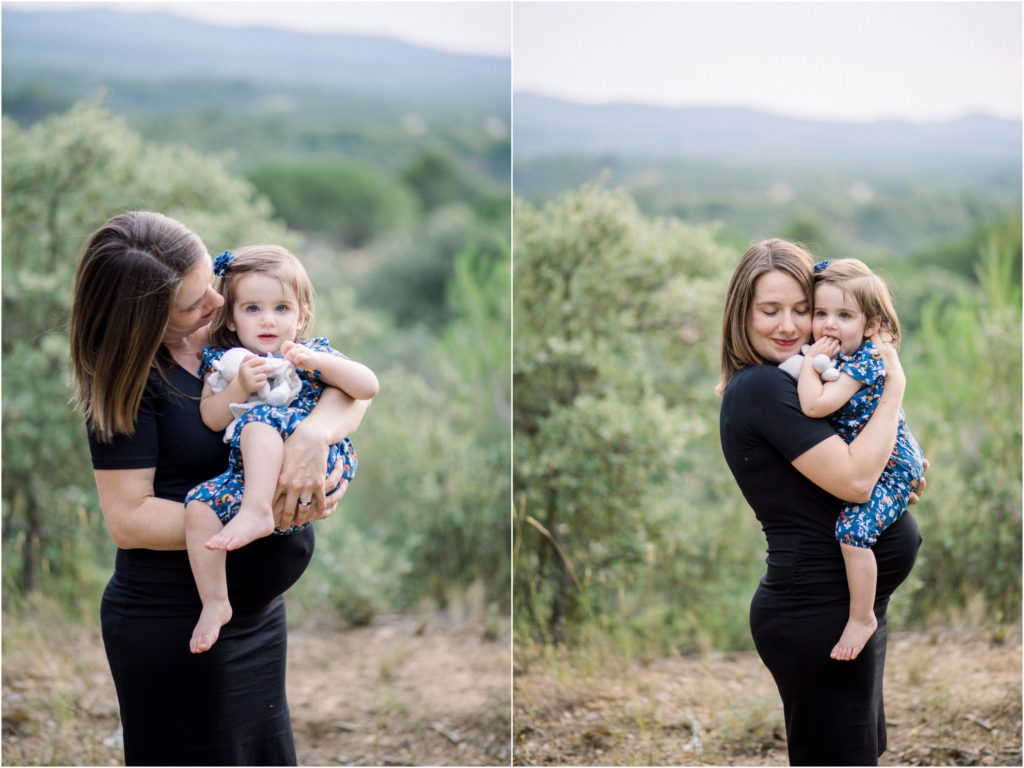 Seance photo grossesse en famille dans la nature, une maman porte sa fille de 18 mois dans les bras